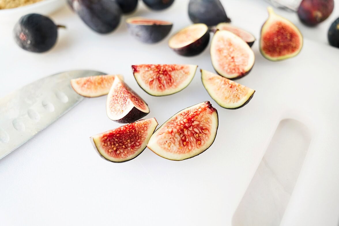 quartered figs on white cutting board with knife in backdrop
