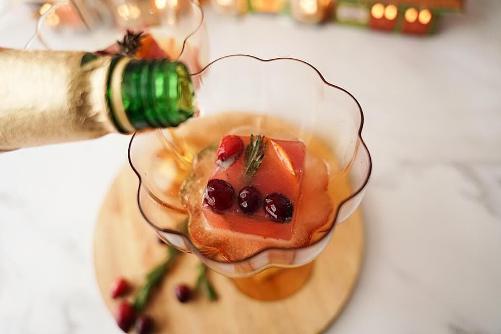 Pouring champagne into glas with the cranberry/orange/rosemary ice cube