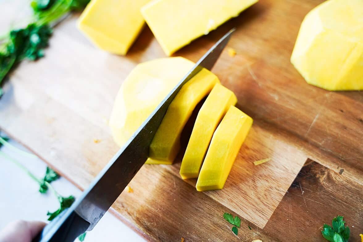 Knife through butternut squash on cutting board into planks