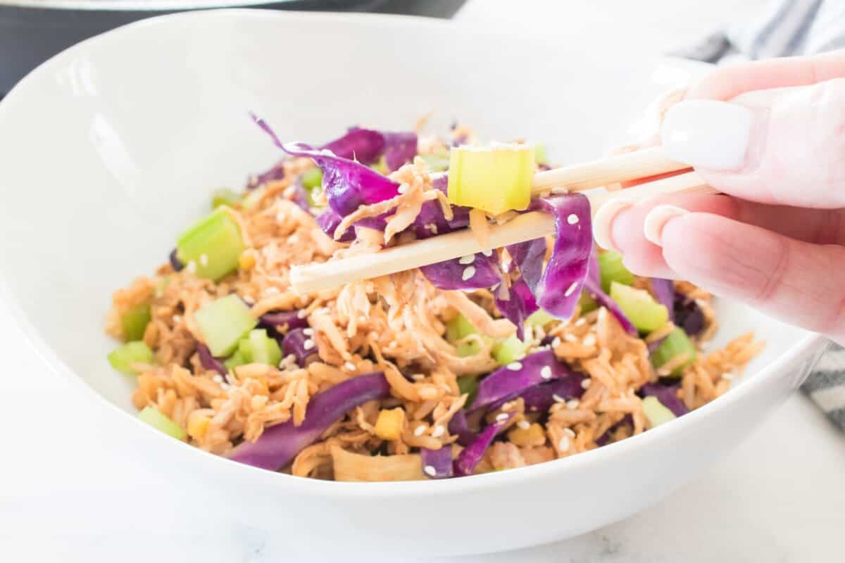 hand holding chop sticks with bite full of chicken egg roll in a bowl above bowl