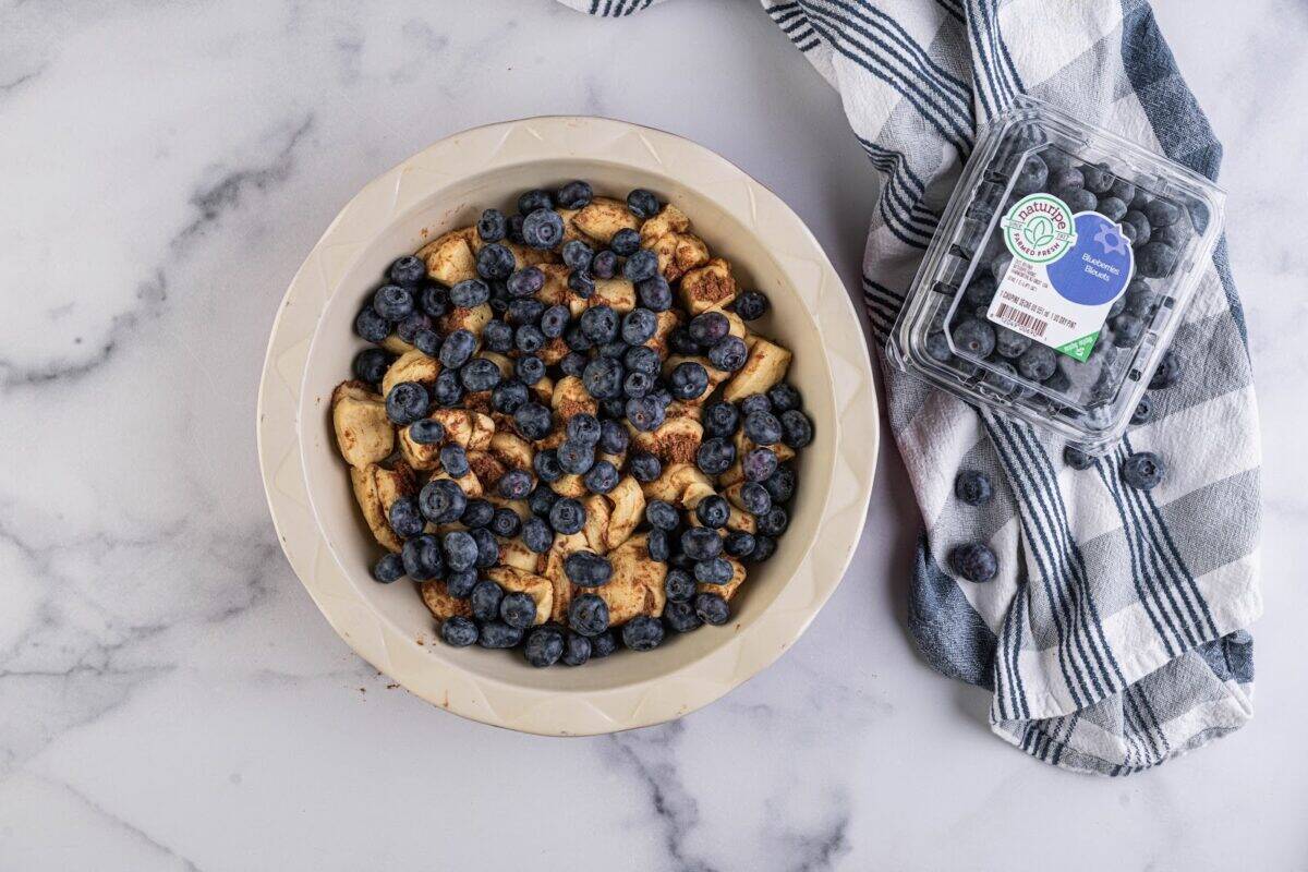 Blueberries sprinkled over cut cinnamon roll dough in a baking pan.