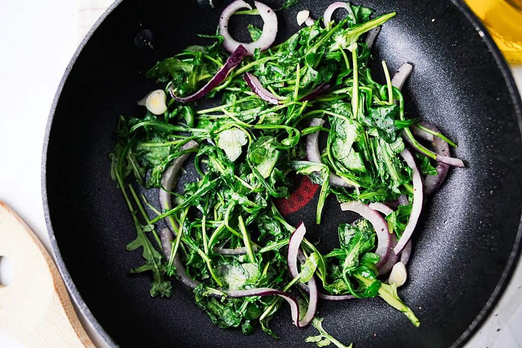 Sauteed arugula in a cast iron sillet with red onions and garlic