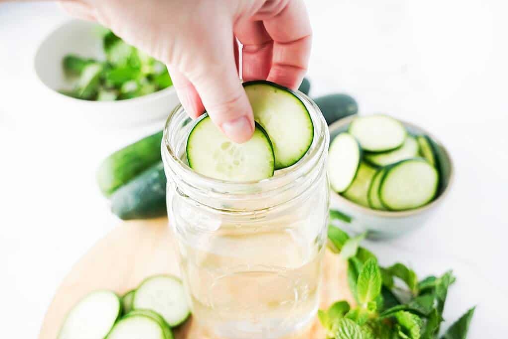 adding cucumber slices to mason jar of water