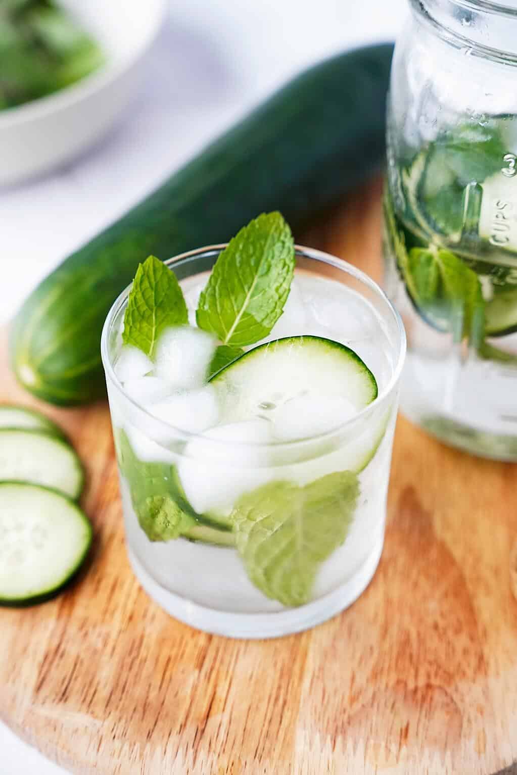 Vertical image of cucumber water in a glass with cucumber in background