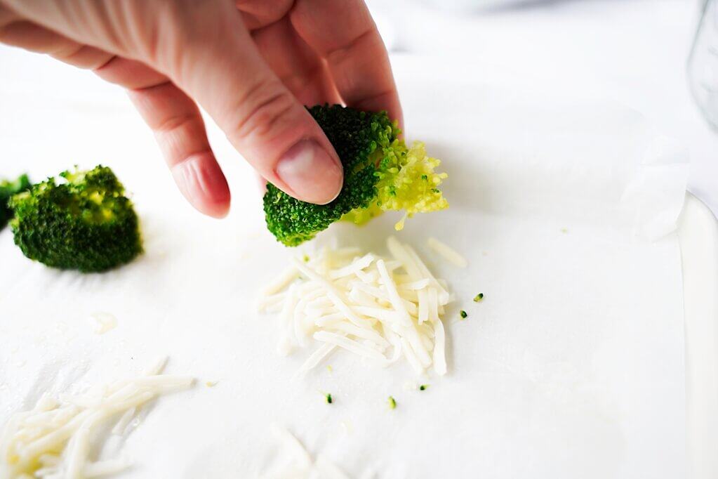 placing broccoli on shredded cheese