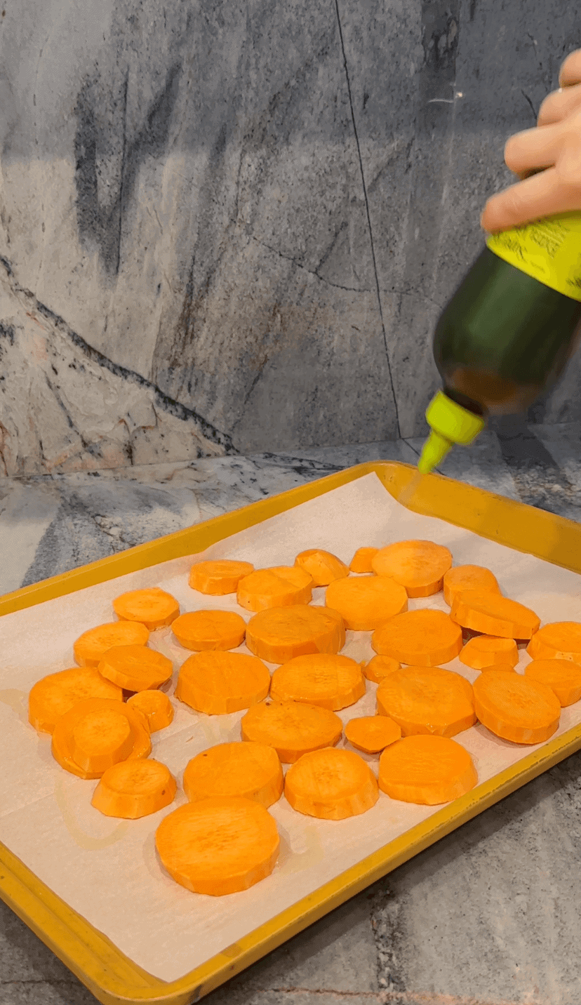 Sweet potato rounds on sheetpan with olive oil being drizzled