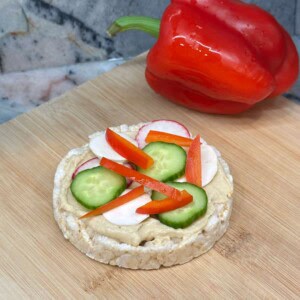 Vertical image of veggie rice cake pizza on a wood cutting board