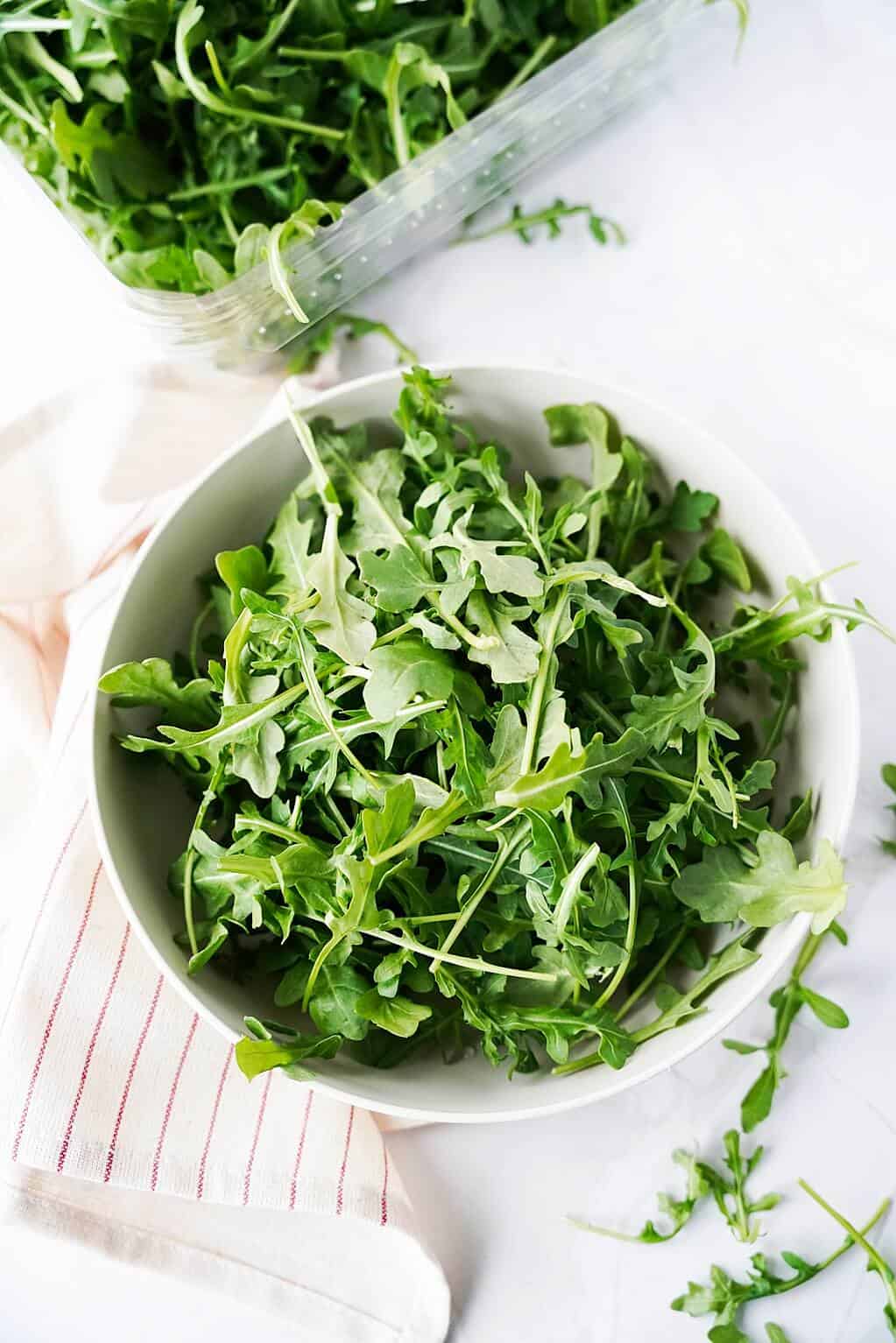 Arugula in a white bowl with clear container above