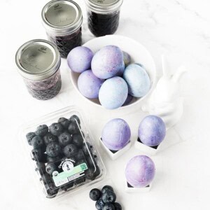 Vertical image of blueberry-dyed hard boiled eggs with jars of blueberry juice and North Bay Produce blueberries