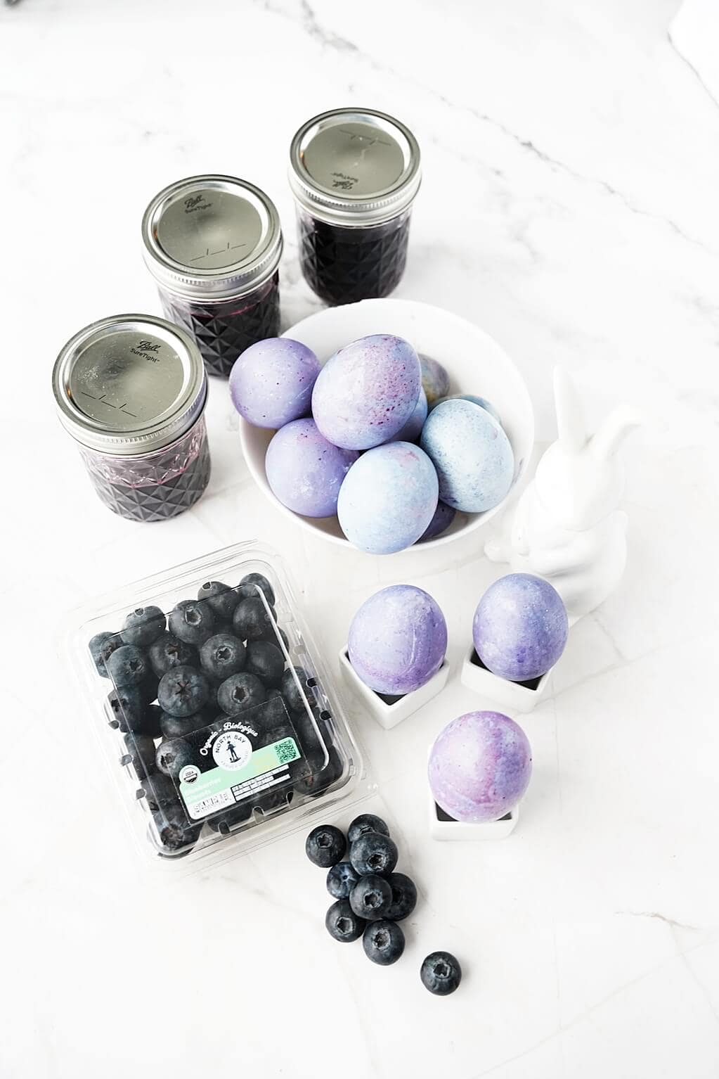 Vertical image of blueberry-dyed hard boiled eggs with jars of blueberry juice and North Bay Produce blueberries