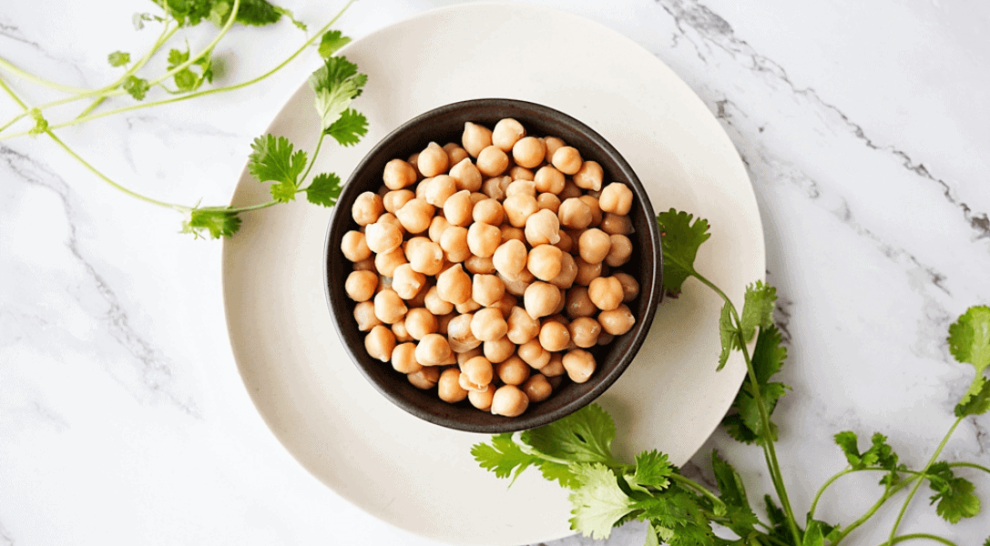 overhead view of chickpeas in a black bowl on a white plate with subtle parsley