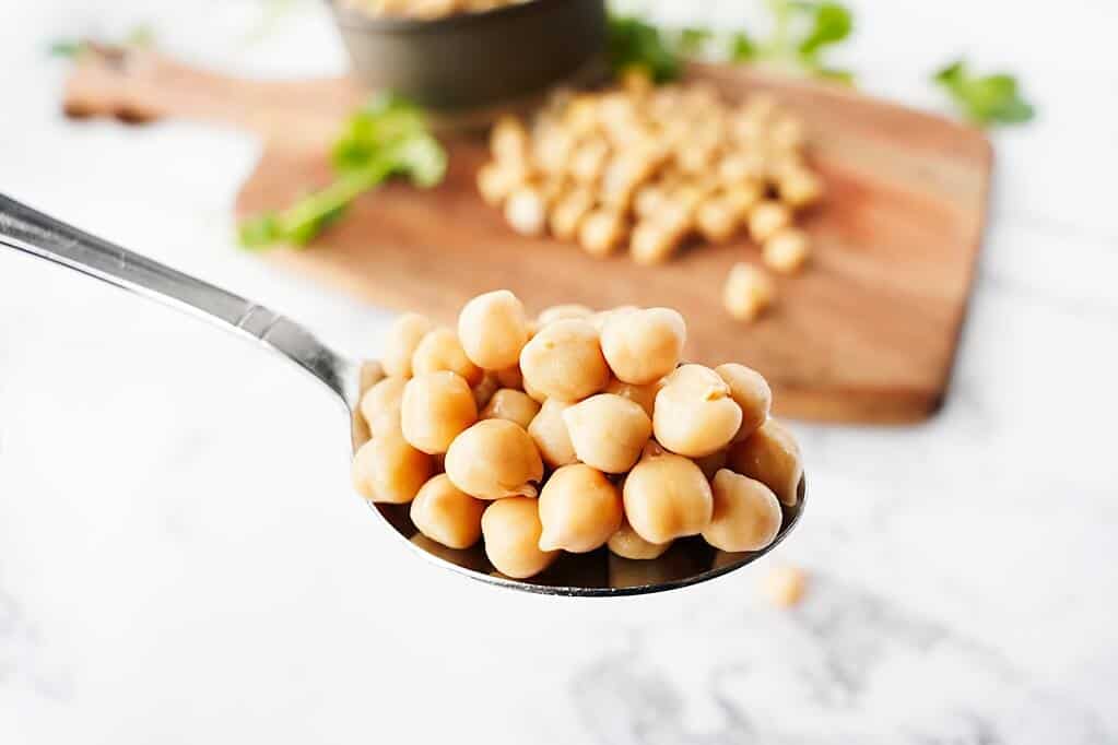 Close up of chickpeas on a spoon with chickpeas on a wooden board in background
