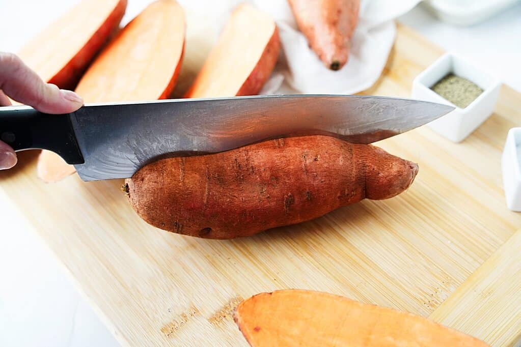 Knife cutting lengthwise into sweet potato on cutting board