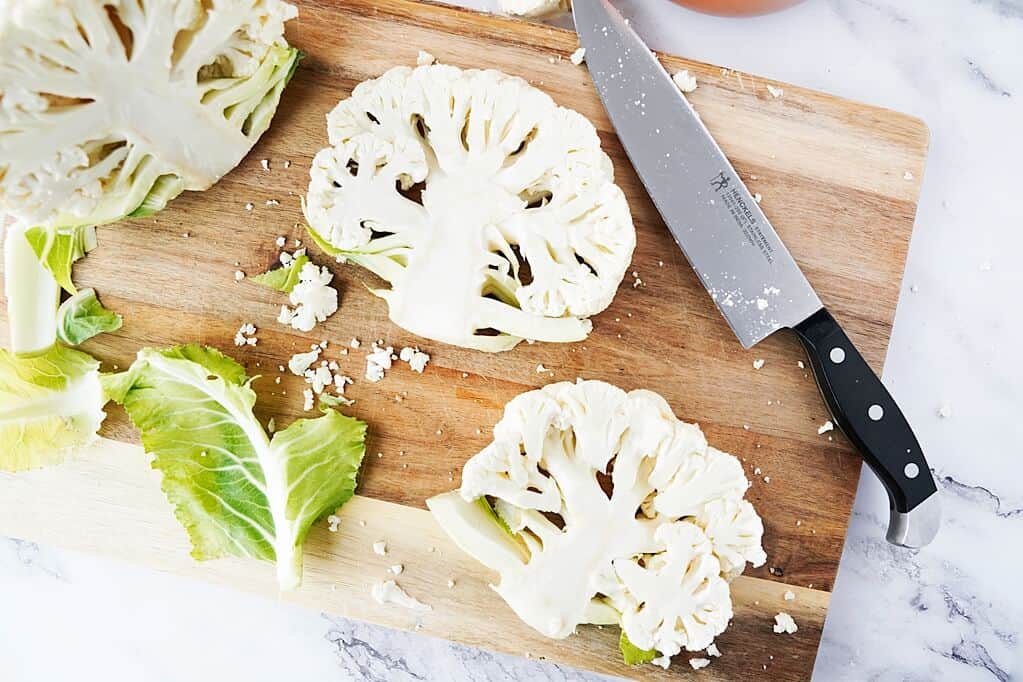 wooden cutting board with knife and 3 cauliflower steaks