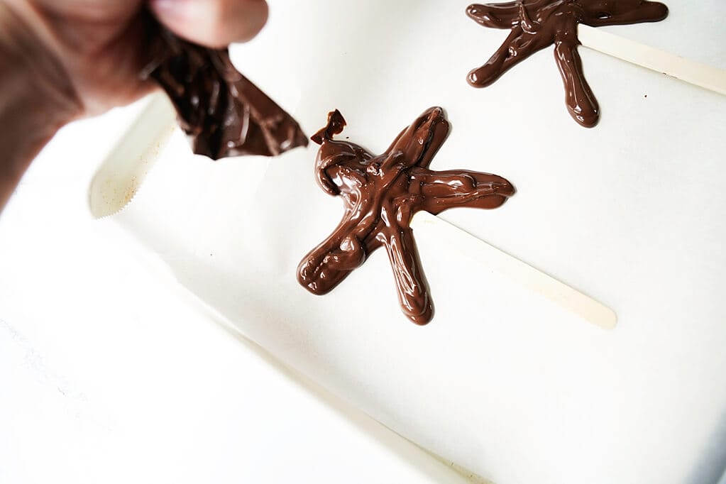 Using the melted chocoalte in piping bags to make star shape on popsicle sticks
