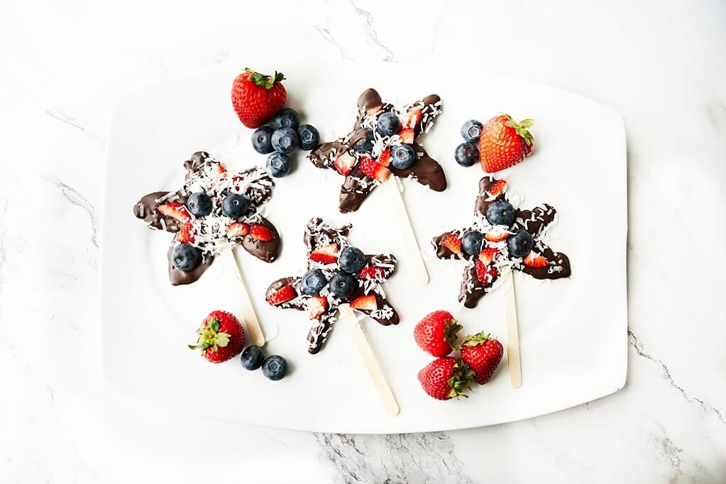 Overhead view of 4 chocolate stars on a white plate with loose strawberries and blueberries