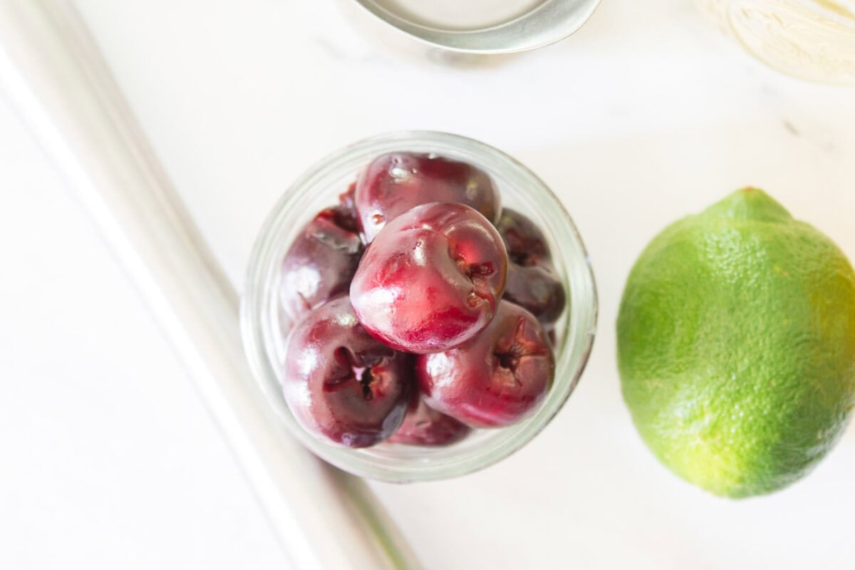 A close-up, top-down shot looking directly into a clear mason jar filled with whole, pitted dark red cherries sitting on a bright marble countertop.
