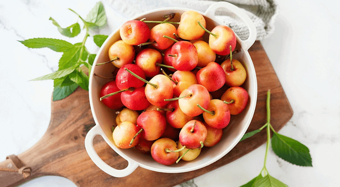 Bowl of Rainier Cherries in white bowl on cutting board