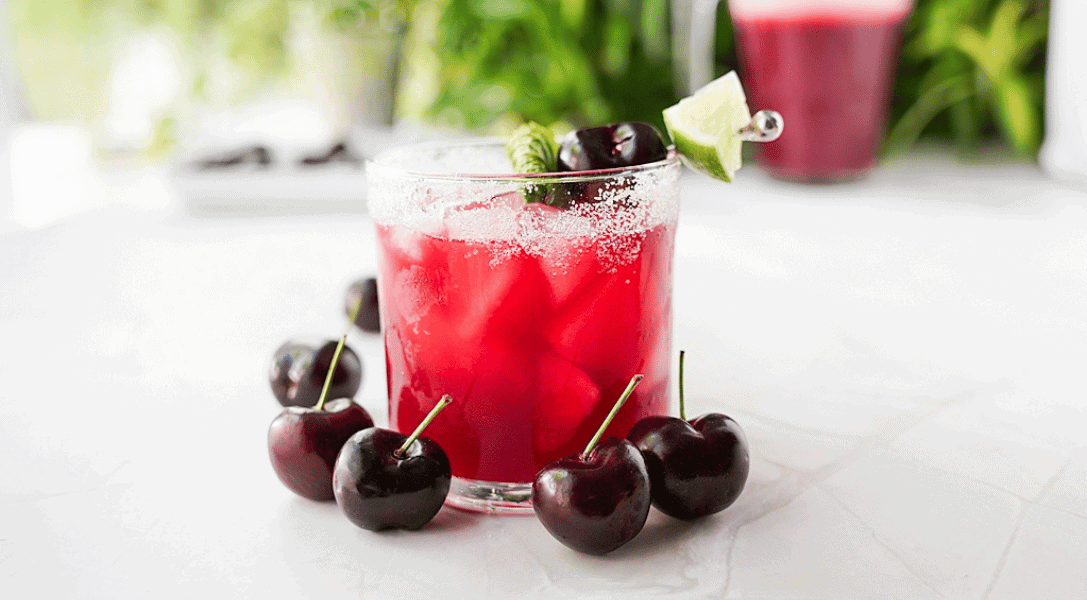 Glass of Homemade Cherry Agua Fresca with Cherries around the glass