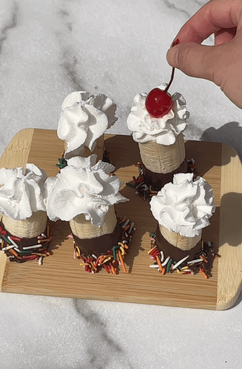Adding whip cream and cherry to the top of the banana split bites