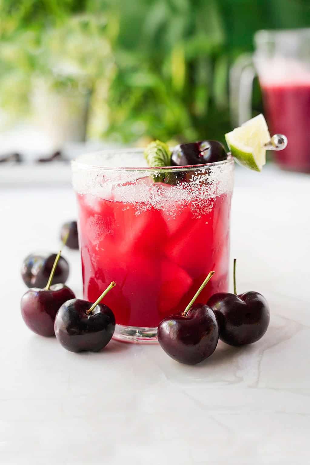 Fresh cherry and lime agua fresca in a glass with fresh cherries in front
