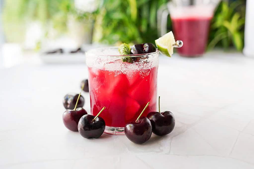 Cherry and lime agua fresca in a glass with lime, mint, and cherry garnish