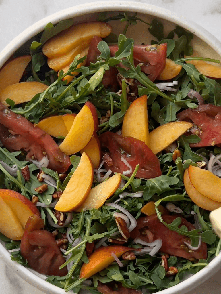 Adding ingredients on the arugula for the peach burrata salad