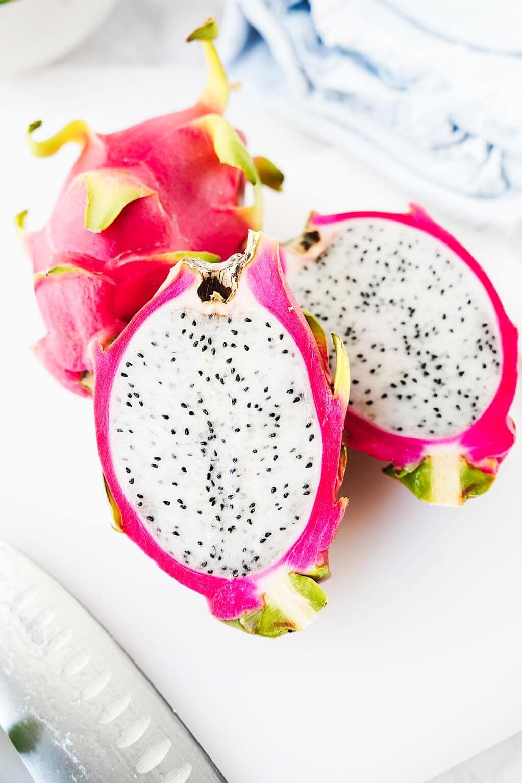 Vertical image of a cut open dragon fruit with the white flesh and whole dragon fruit in the background