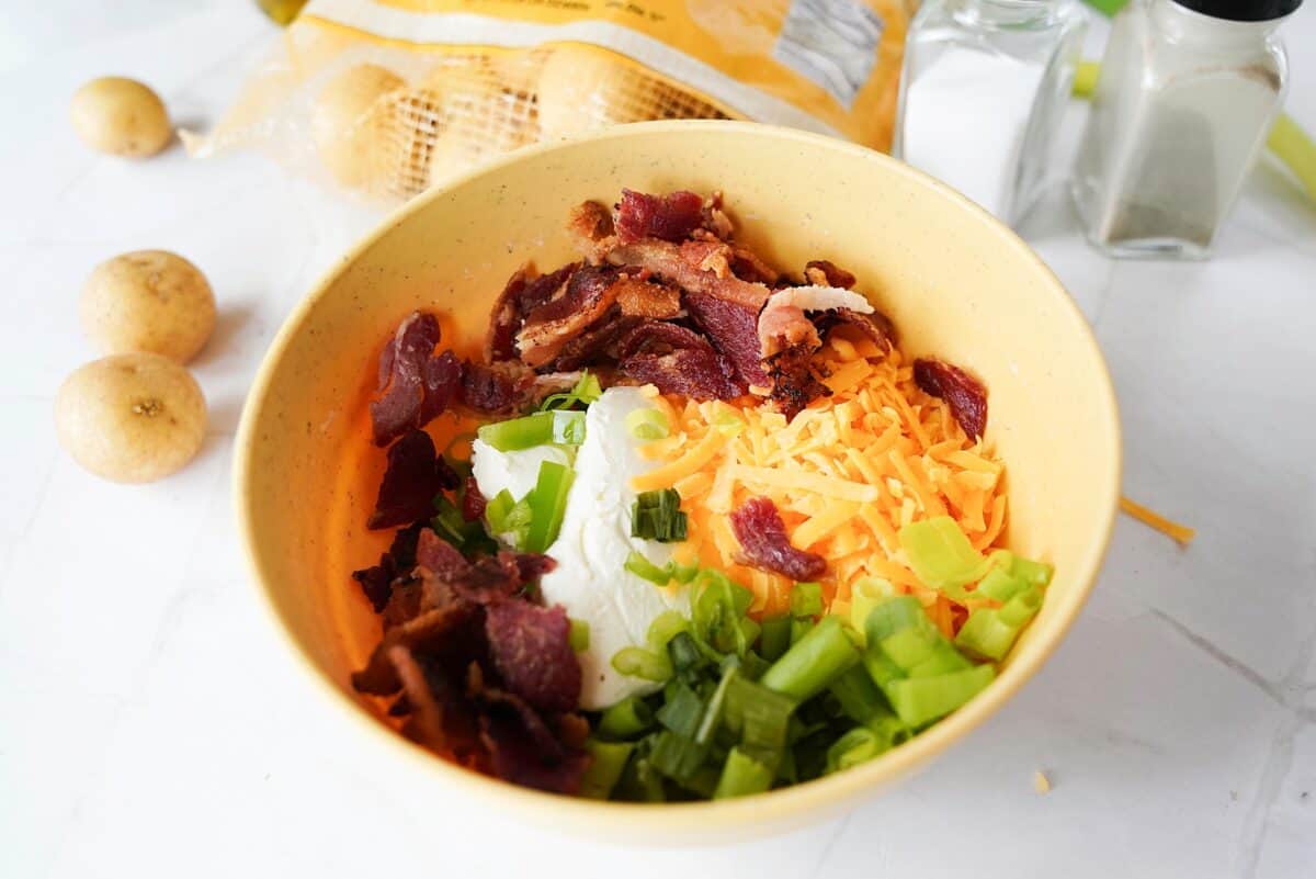 Cream cheese, cheddar cheese, sliced green onion, and crumbled bacon in a bowl.